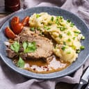 A pork roast and mash potatoes with tomato and herbs on a plate