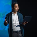 A young man holding a lap top and giving a presentation