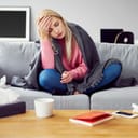 A young woman feeling sick sitting on a couch, holding her hand on her forehead