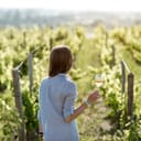 Young woman with wine glass standing on the beautiful vineyard during the sunset