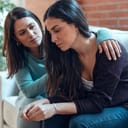 Shot of pretty young woman supporting and comforting her sad friend while sitting on the sofa at home.