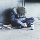 Homeless man sitting on the street in the shadow of the building and begging for help and money. Problems of big modern cities.
