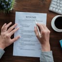 A resume on table being inspected by a person holding a pencil