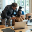 A team lead talking with an employee sitting at the desk and looking at his tablet