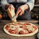 Person grating cheese onto a pizza