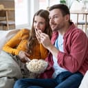couple enjoying a movie while eating popcorn on the sofa at home