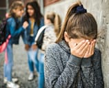 Sad elementary age schoolgirl covering her face next to her peers