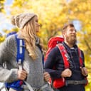 adventure, travel, tourism, hike and people concept - smiling couple walking with backpacks over autumn natural background