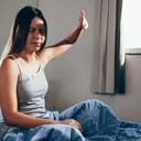 young girl in the bed looking upset after waking up bothered by the morning light