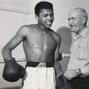 A vintage shot of Muhammad Ali wearing boxing equipment inside a ring next to another man