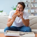 A man sitting on a couch enjoying a slice of pizza