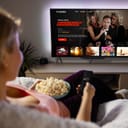 Woman sitting on sofa with a bowl of popcorn in her lap browsing a streaming service