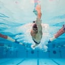A professional male swimmer glides gracefully underwater in a swimming pool.