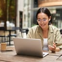 young woman participating in an online meeting from an outdoor café, working remotely while drinking coffee