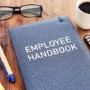 Notebook titled 'employee handbook' lying on the table among other stationery