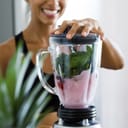 Woman blending spinach, berries, bananas and almond milk to make a healthy green smoothie