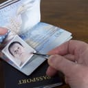 Hand with tweezers holding id photo over passport as if forging the travel documents