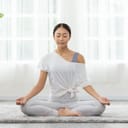 young Asian woman practicing yoga with lotus pose on a carpet in a cozy white room