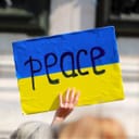 A person holding a board with the colors of the Ukrainian flag with the works 'peace' on it