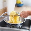 A closeup of a person straining pasta through a colander