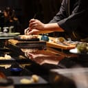 A closeup of a sushi chef preparing a meal on a wooden board at a restaurant 