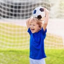 Cheerful small boy at soccer practice holding a deflated ball over his head