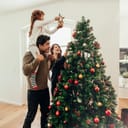 Family decorating a Christmas tree. Young man with his daughter on his shoulders helping her decorate the Christmas tree.