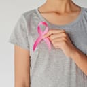 A girl in grey t-shirt holding a pink ribbon across her chest