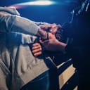 Close-up of a male police officer aggressively handcuffing a civilian on the hood of a police car.