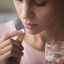 A woman taking a tablet of medicine with a glass of water