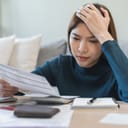 stressed young woman at home calculating taxes and expenses with credit card bills spread on the table