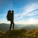 A person with a backpack standing on top of a hill watching the sunset