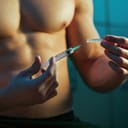 close-up of a muscular athlete in locker room with a syringe, implying the use of performance-enhancing drugs