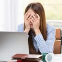 Distressed woman covering her face with hands in front of a laptop