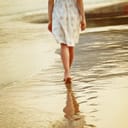 Woman walking barefoot on sand near water