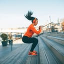 A young woman with orange headphones wearing an orange-black tracksuit exercising