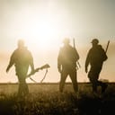 Three hunters walking across a field against a sunset background