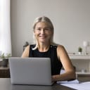 Businesswoman sitting at her desk, working on her laptop and smiling at the camera.