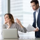 Woman dismissively pointing her hands while looking away towards a man who is trying to talk to her and show her a piece of paper