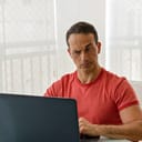 A man sitting at table looking at his laptop in a distrusting fashion