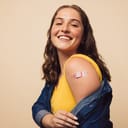 Smiling woman exposing her bandaged arm after receiving vaccination.