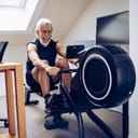 senior man using a rowing machine in his home office