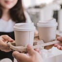 A person taking two disposable coffee cups from a coffee shop clerk