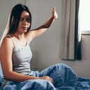 young girl waking up, annoyed by the morning light while sitting on her bed