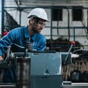 A man wearing a working suit and a helmet working a machine at a factory