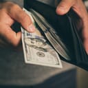 A person taking out money out of a leather wallet