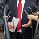 A man in a suit with a red tie holding a press conference