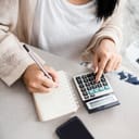 woman writing a list of debt on notebook calculating her expenses with calculator with many invoices , female hand doing accounting