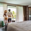 back view of young traveling couple opening the hotel room curtains to enjoy the view