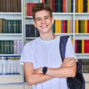 A smiling student carrying an backpack on one shoulder in a library